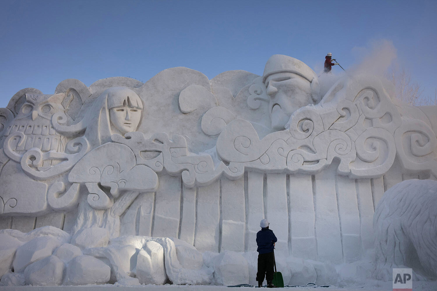 Two workers remove fresh snow piled on a large snow sculpture at the annual Sapporo Snow Festival, Feb. 4, 2020, in Sapporo, Hokkaido, Japan. (AP Photo/Jae C. Hong)