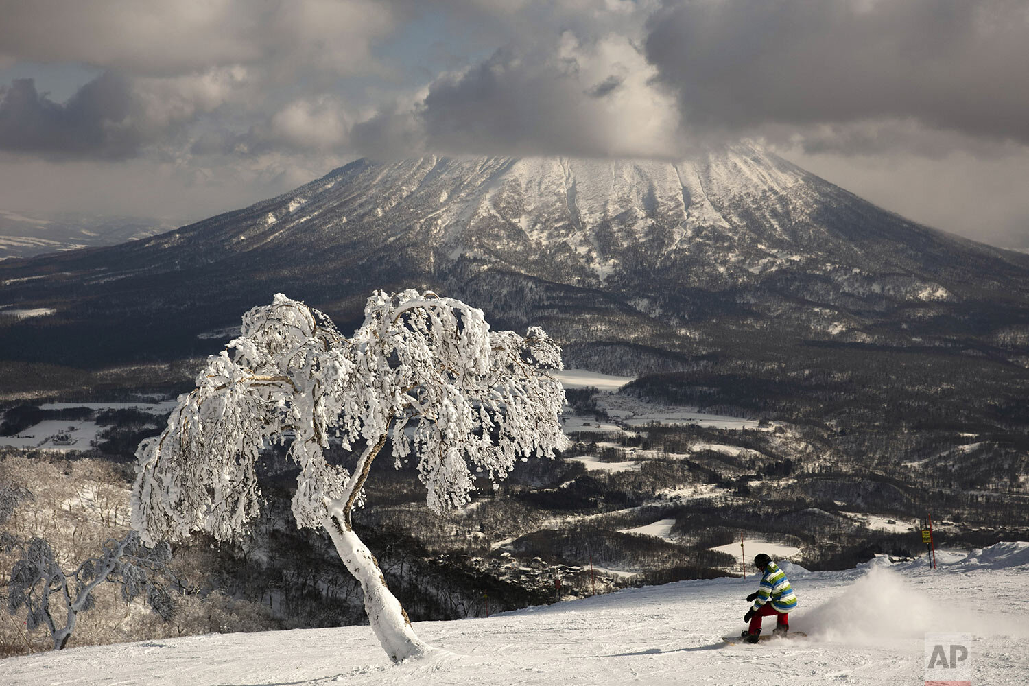 A man snowboards down a slope overlooking Mount Yotei at a ski resort Wednesday, Feb. 5, 2020, in Niseko, Hokkaido, Japan. (AP Photo/Jae C. Hong)