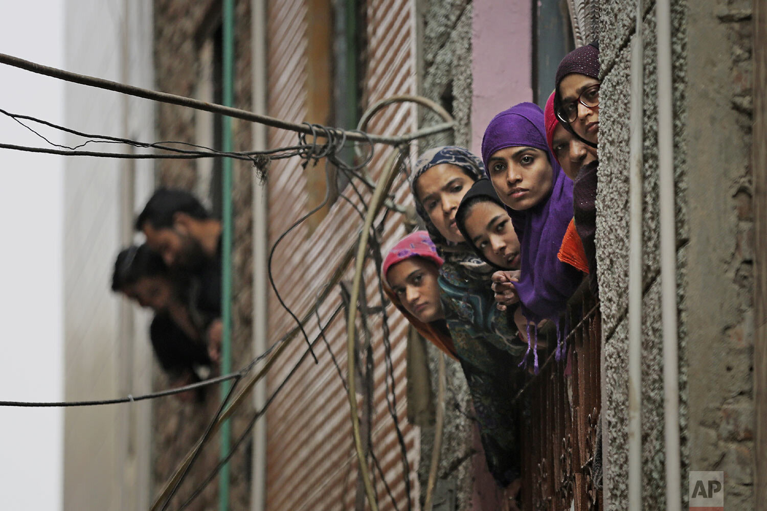Indian Muslim women look out of a window as security officers patrol a street in New Delhi, India, Wednesday, Feb. 26, 2020. (AP Photo/Altaf Qadri)