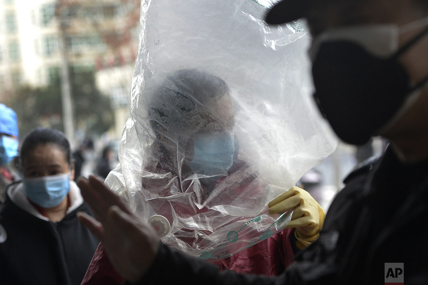 A man wearing a protective face mask covered himself with a plastic cover before enters a supermarket in Wuhan in central China's Hubei province, Monday, Feb. 10, 2020. (Chinatopix via AP)