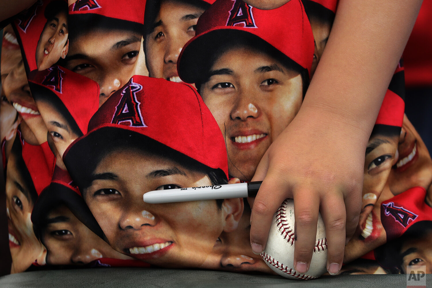  A fan holds a baseball against his shirt covered with images of Los Angeles Angels' Shohei Ohtani as he waits for autographs before a spring training baseball game between the Los Angeles Angels and the Texas Rangers Friday, Feb. 28, 2020, in Tempe,