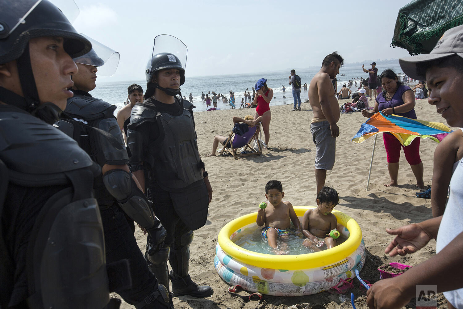  Boys sit in an inflatable pool while eating green sugar-coated apples as policemen work to remove an unlicensed food vendor, at Agua Dulce beach in Lima, Peru, Feb. 15, 2020. (AP Photo/Rodrigo Abd) 