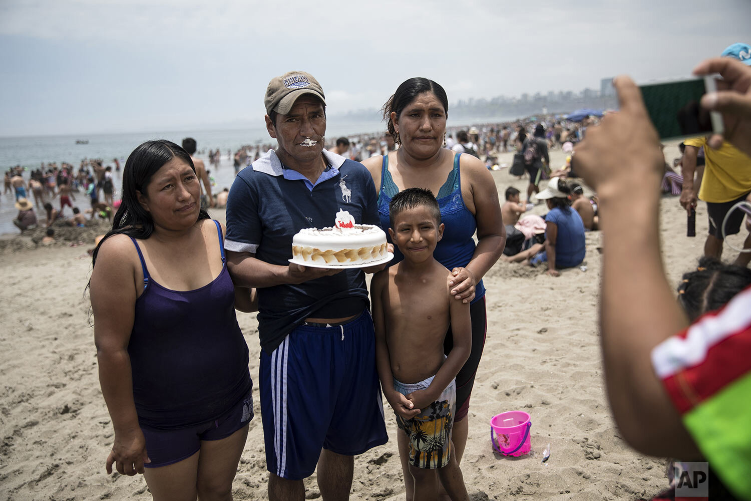  A man, holding his birthday cake, poses for a photo with his family on the shore of Agua Dulce beach in Lima, Peru, Feb. 23, 2020. (AP Photo/Rodrigo Abd) 