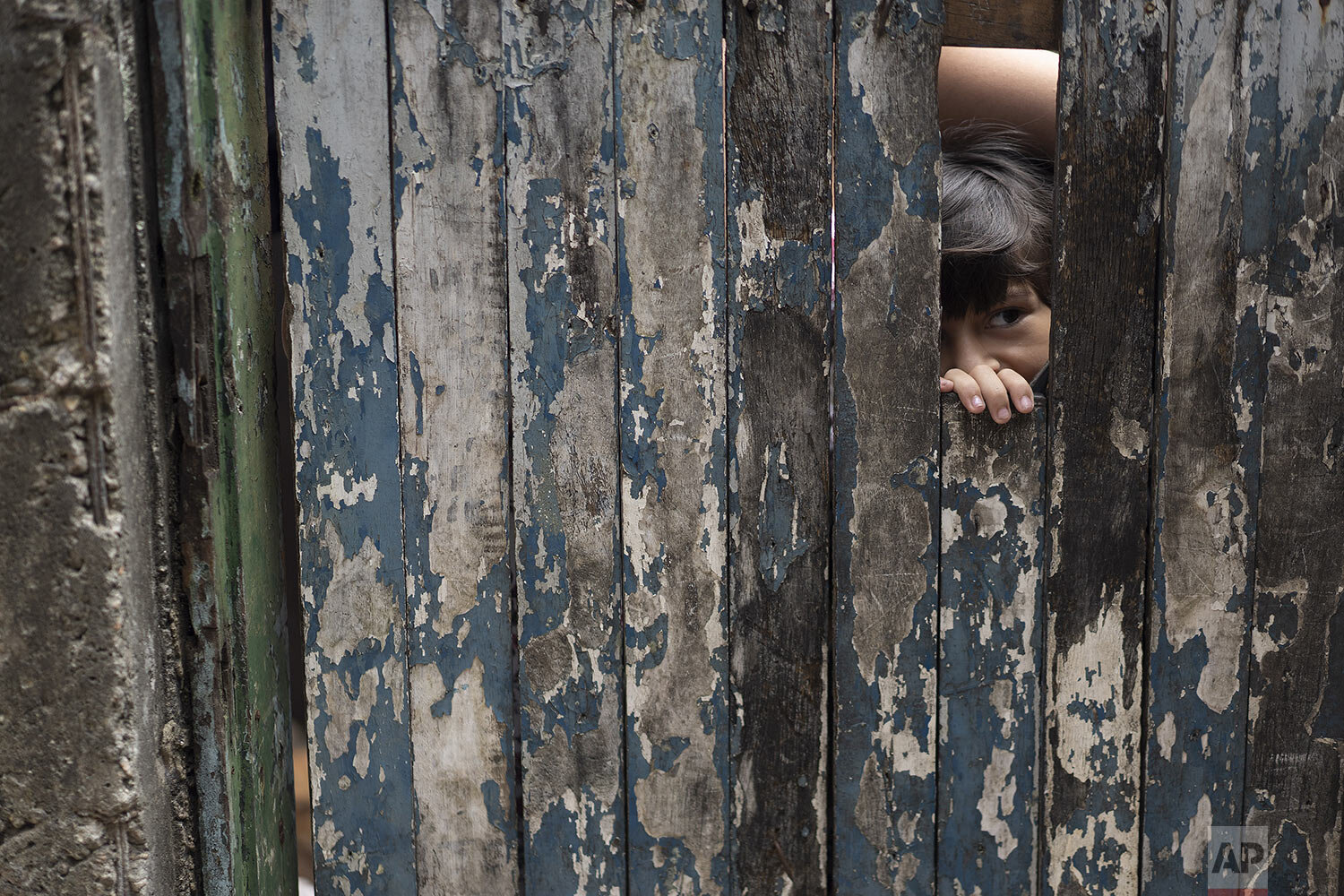  A boy peaks from the dilapidated doorway of his home as his mother receives soap and detergent from volunteers as an effort to avoid the spread of the new coronavirus, in the Rocinha slum of Rio de Janeiro, Brazil, March 24, 2020. (AP Photo/Leo Corr