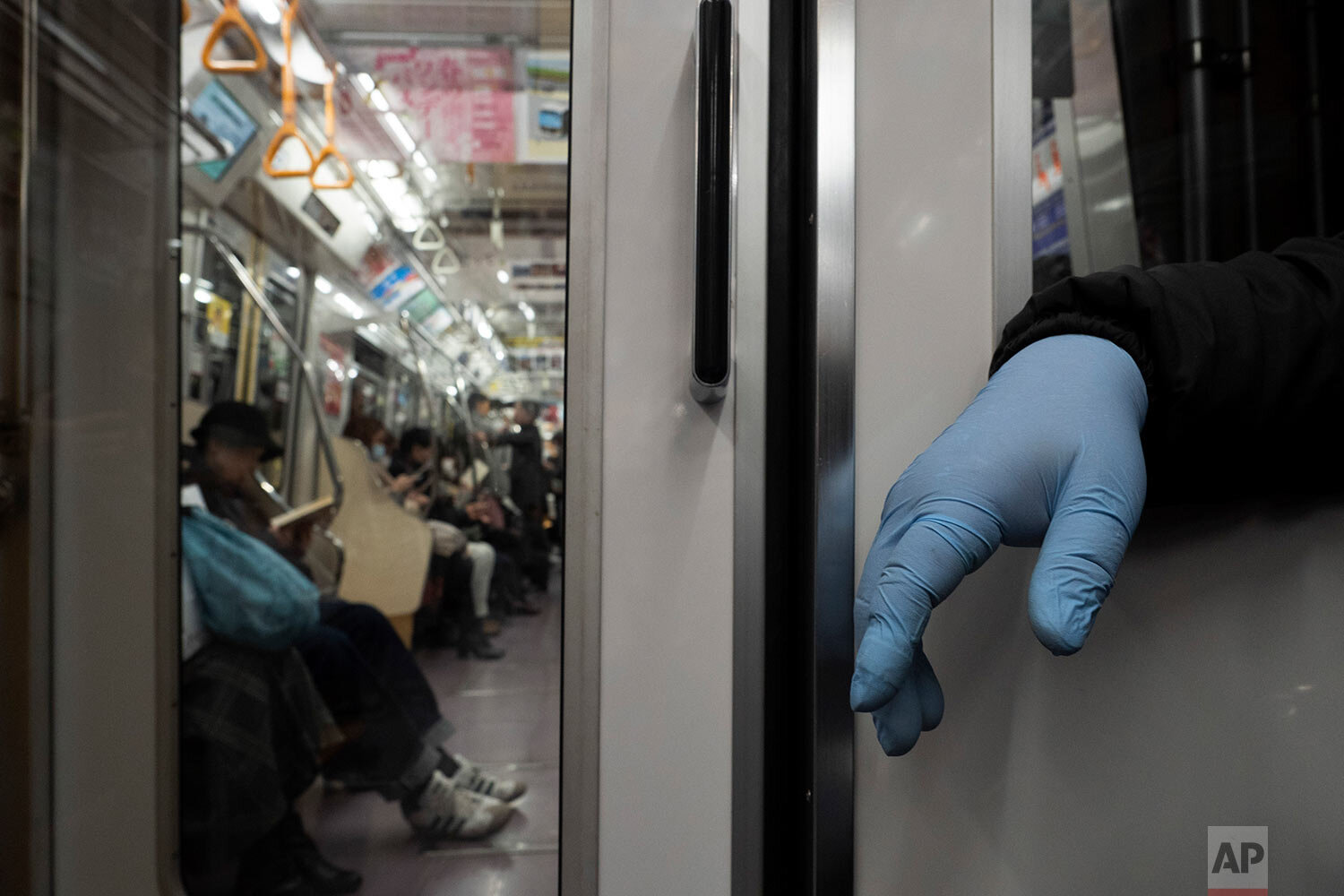  A man wearing a protective glove sits in a train in Tokyo, Monday, March 16, 2020. (AP Photo/Jae C. Hong) 