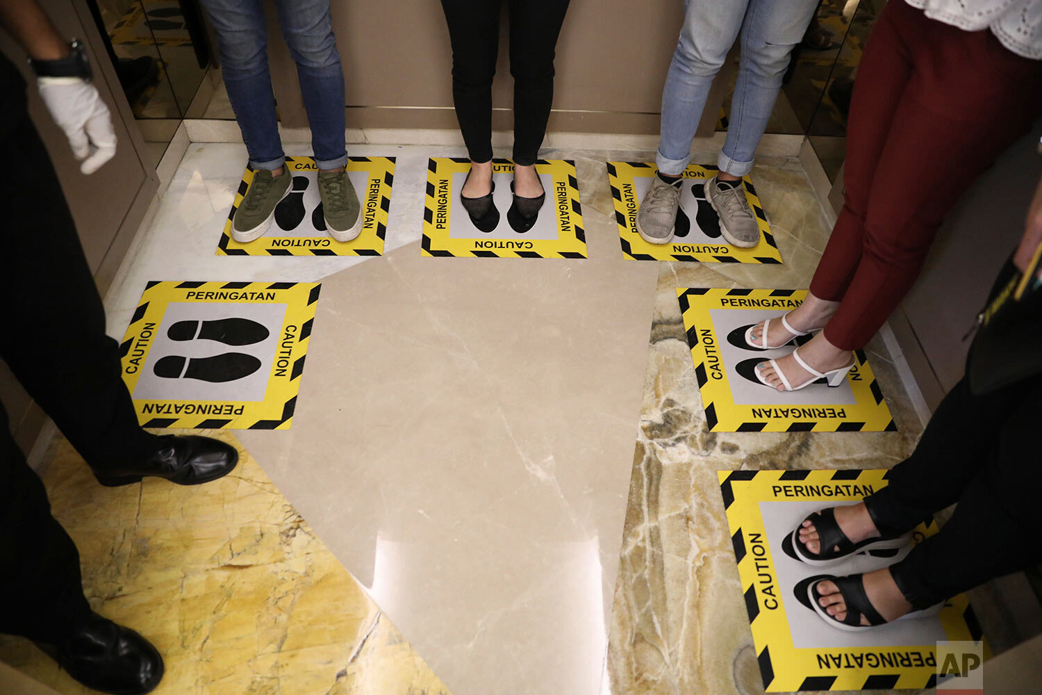  People stand in designated areas on the floor of an elevator as a social distancing effort to prevent the spread of the new coronavirus at a shopping mall in Surabaya, Indonesia, Thursday, March 19, 2020.  (AP Photo/Trisnadi) 
