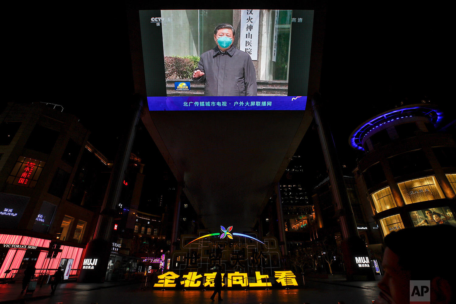  People walk by a giant TV screen broadcasting news of Chinese President Xi Jinping talking to medical workers at the Huoshenshan Hospital in Wuhan in central China's Hubei Province, at a quiet shopping mall in Beijing, Tuesday, March 10, 2020. (AP P