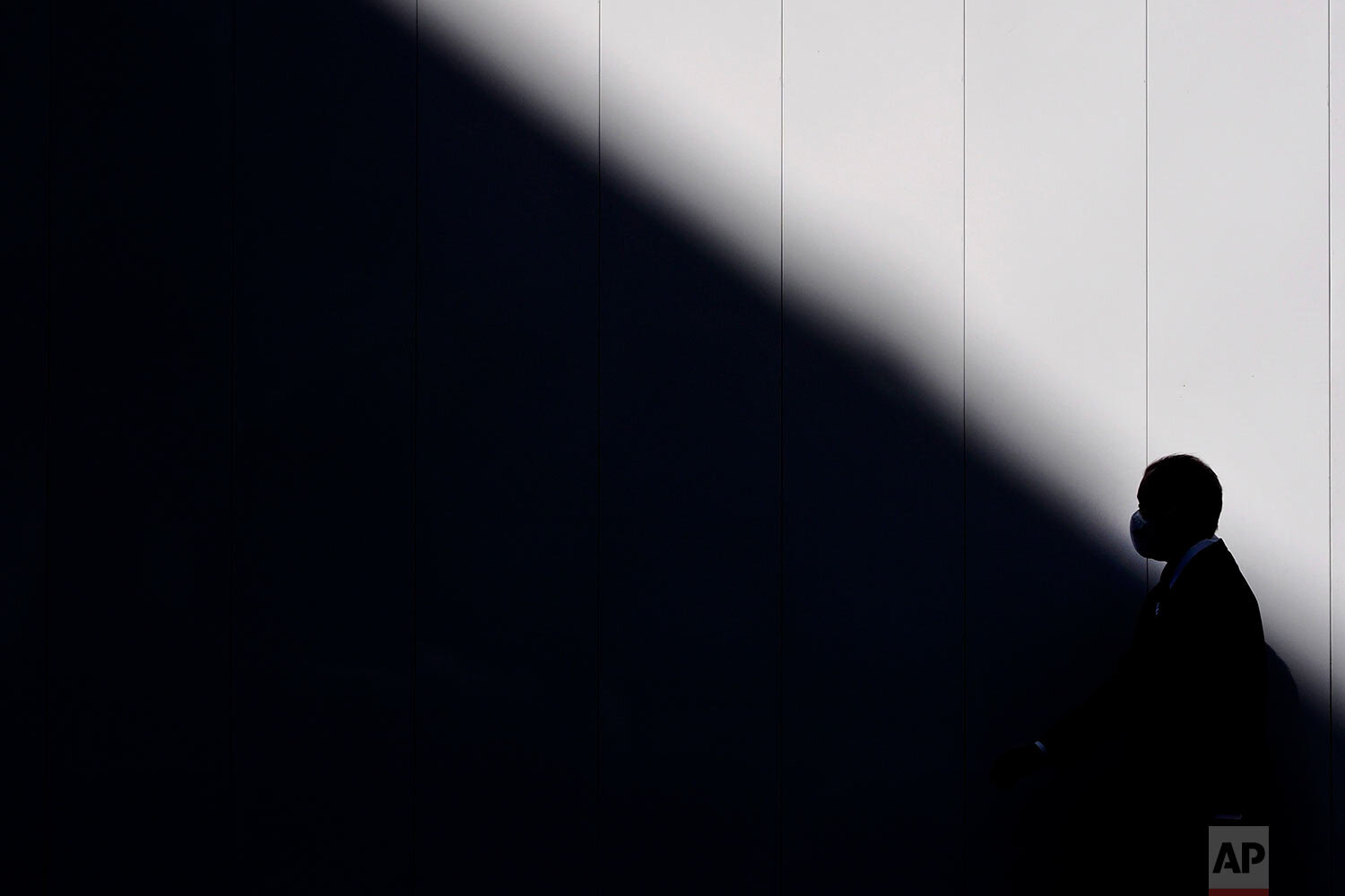  A man wearing a mask is silhouetted against a wall as he walks into the shade of a building Thursday, March 26, 2020, in Tokyo. (AP Photo/Jae C. Hong) 