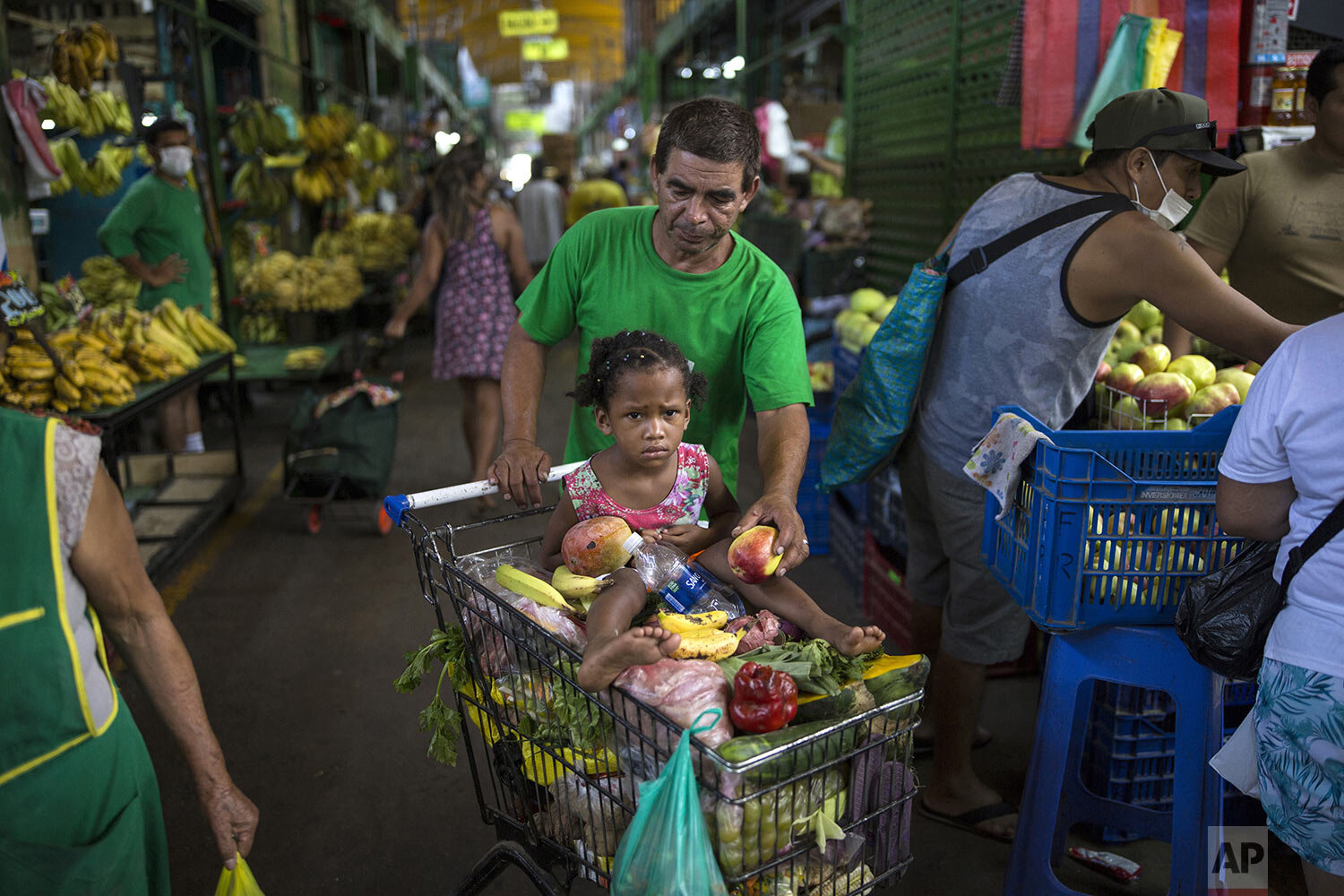  In this March 18, 2020 photo, Cesar Alegre, accompanied by his 4-year-old daughter Lia, places a damaged apple in his shopping cart filled with discarded produce given to him by vendors at a popular market in Lima, Peru.  (AP Photo/Rodrigo Abd) 