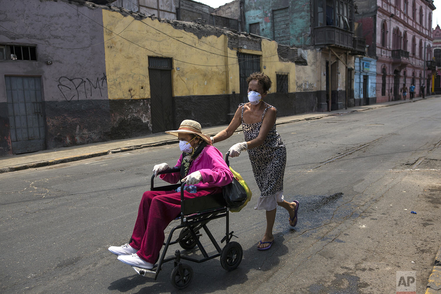  In this March 18, 2020 photo, Flor Vaso pushes her 84-year-old mother Carmen Reyes in a wheelchair to their home, a large, deteriorated house near the presidential palace that has earned it the nickname “Luriganchito,” or “Little Lurigancho,” after 