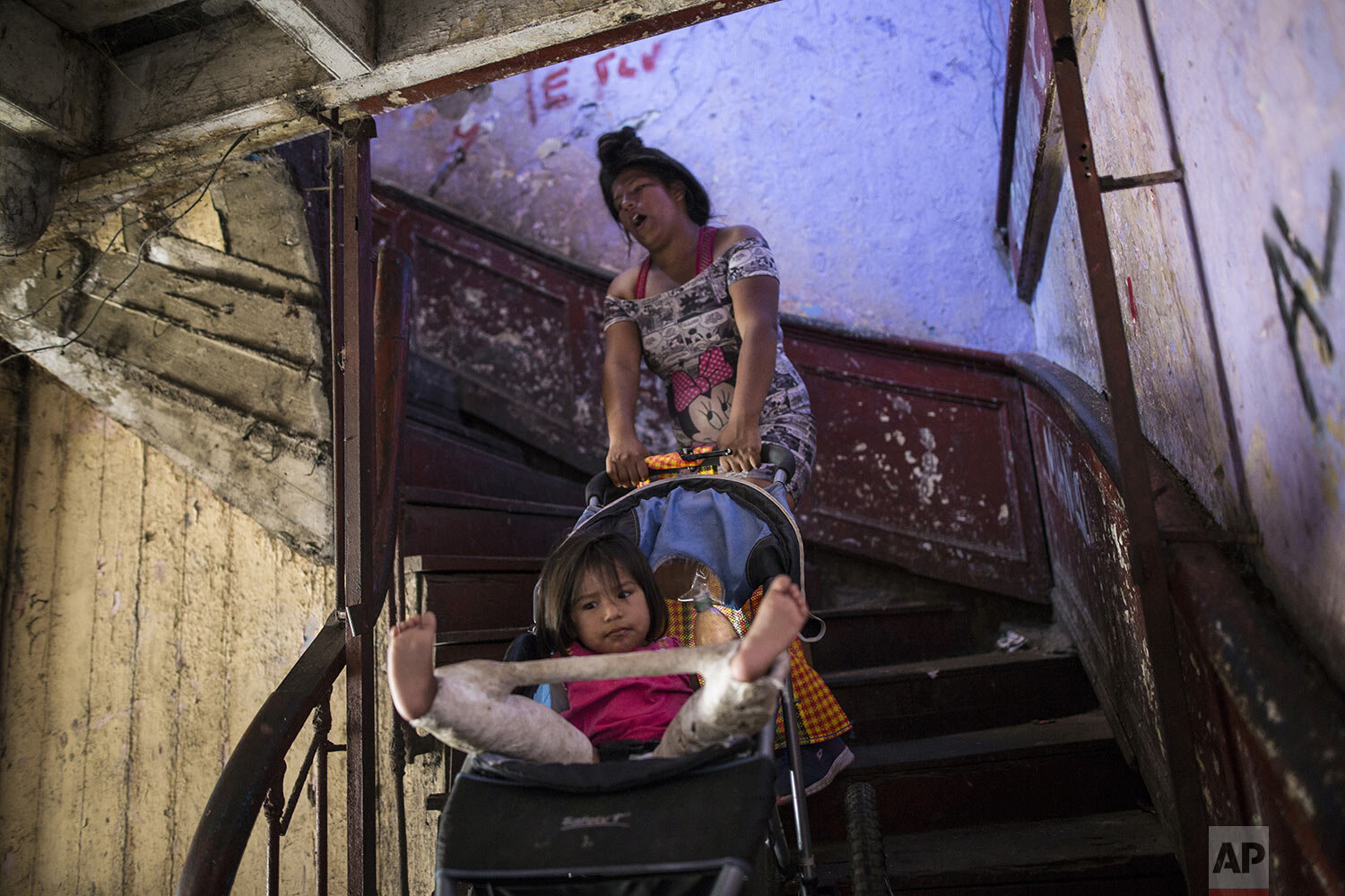  In this March 18, 2020 photo, Nilu Asca, a 24-year-old single mother, struggles to pull a stroller holding her 2-year-old daughter Darleth up a flight of stairs, inside a building nicknamed “Luriganchito,” after the country’s most populous prison, i