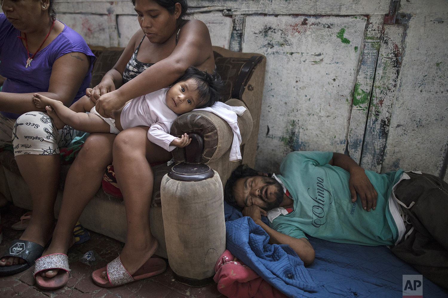  In this March 29, 2020 photo, Ivonne Garcia changes her daughter's diaper in her small room while her homeless cousin naps nearby, in the deteriorating building nicknamed "Luriganchito," after the country's most populous prison, in Lima, Peru. (AP P