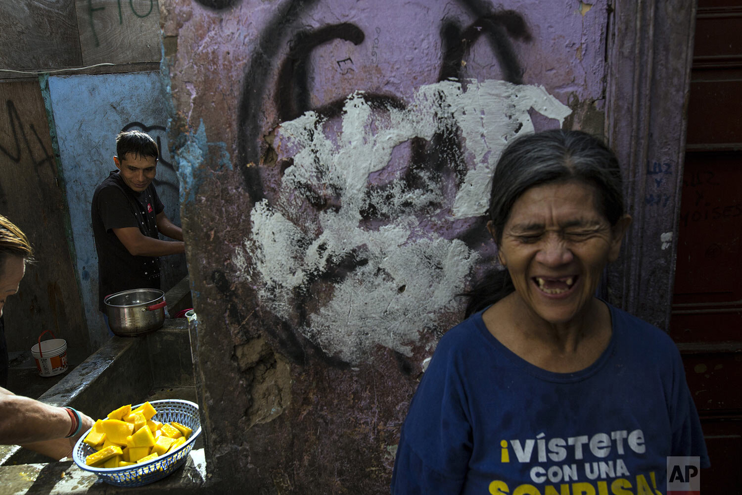  In this March 19, 2020 photo, Nelida Rojas, wearing a T-shirt emblazoned with a message that reads in Spanish: "Dress yourself with a smile", laughs as she jokes with fellow residents as she waits her turn to use the communal laundry area, inside a 