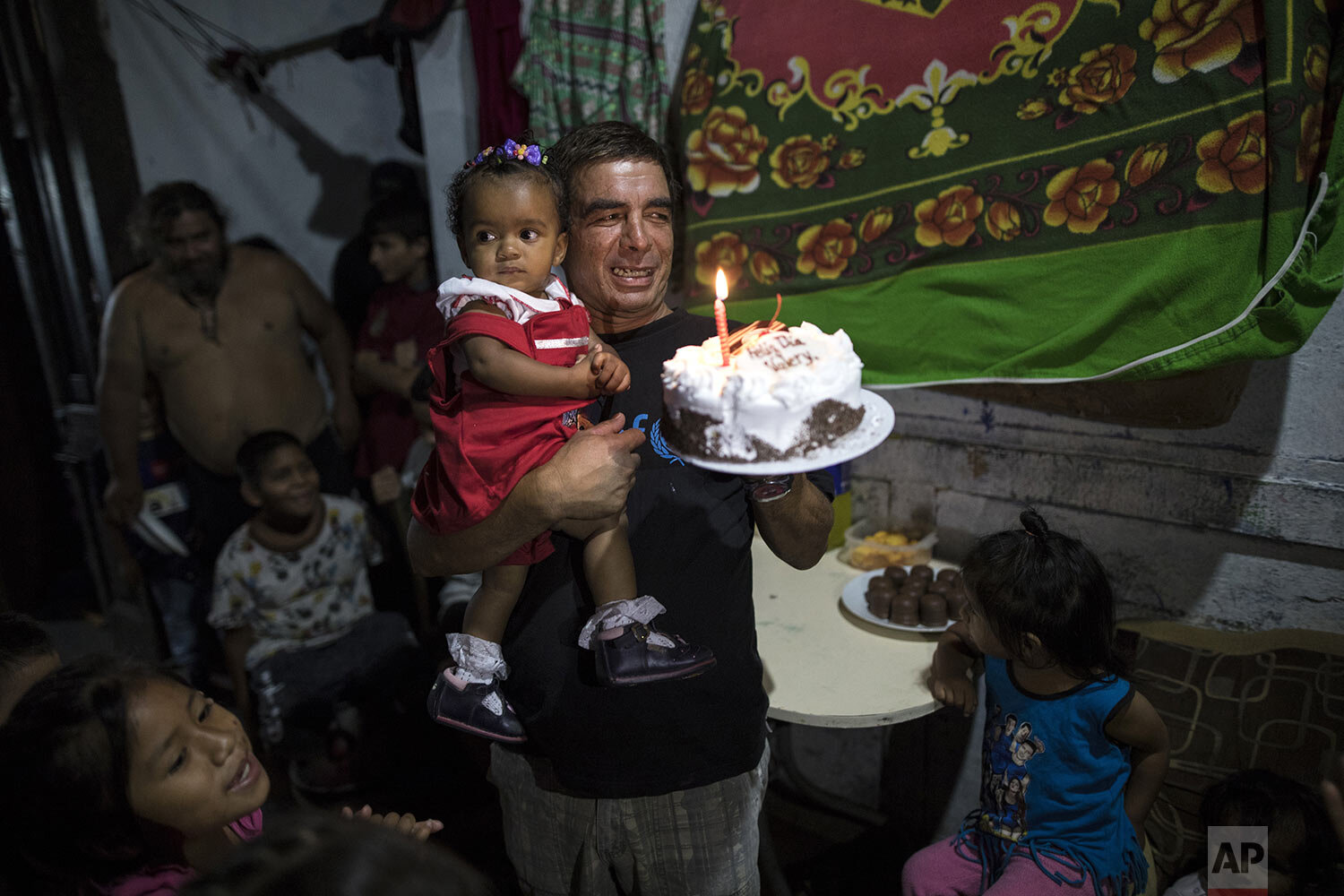  In this March 18, 2020 photo, Cesar Alegre carries his daughter Valerie while holding her store bought cake, as he and fellow residents prepare to mark her first birthday in the deteriorating building where they live, nicknamed “Luriganchito,” after