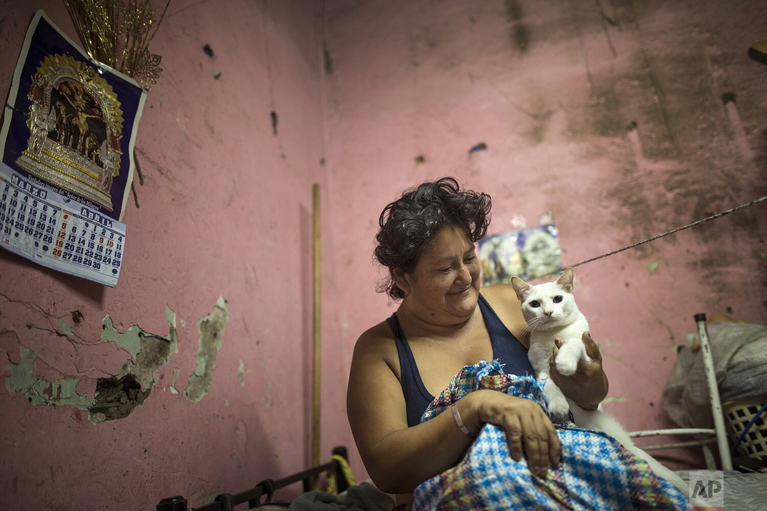  In this April 3, 2020 photo, Zulema Aguinaga smiles at her pet cat as she starts the day inside her small room she shares with her son and elderly aunt, in a deteriorated house nicknamed “Luriganchito,” after the country’s most populous prison, in L