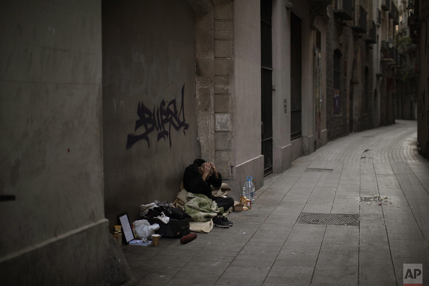 In this Saturday, March 21, 2020, Javier Redondo, 40, covers his head with his hands as he waits for alms on an empty street of Barcelona, Spain. While authorities are telling people to stay at home amid the COVID-19 outbreak, others as Javier are h