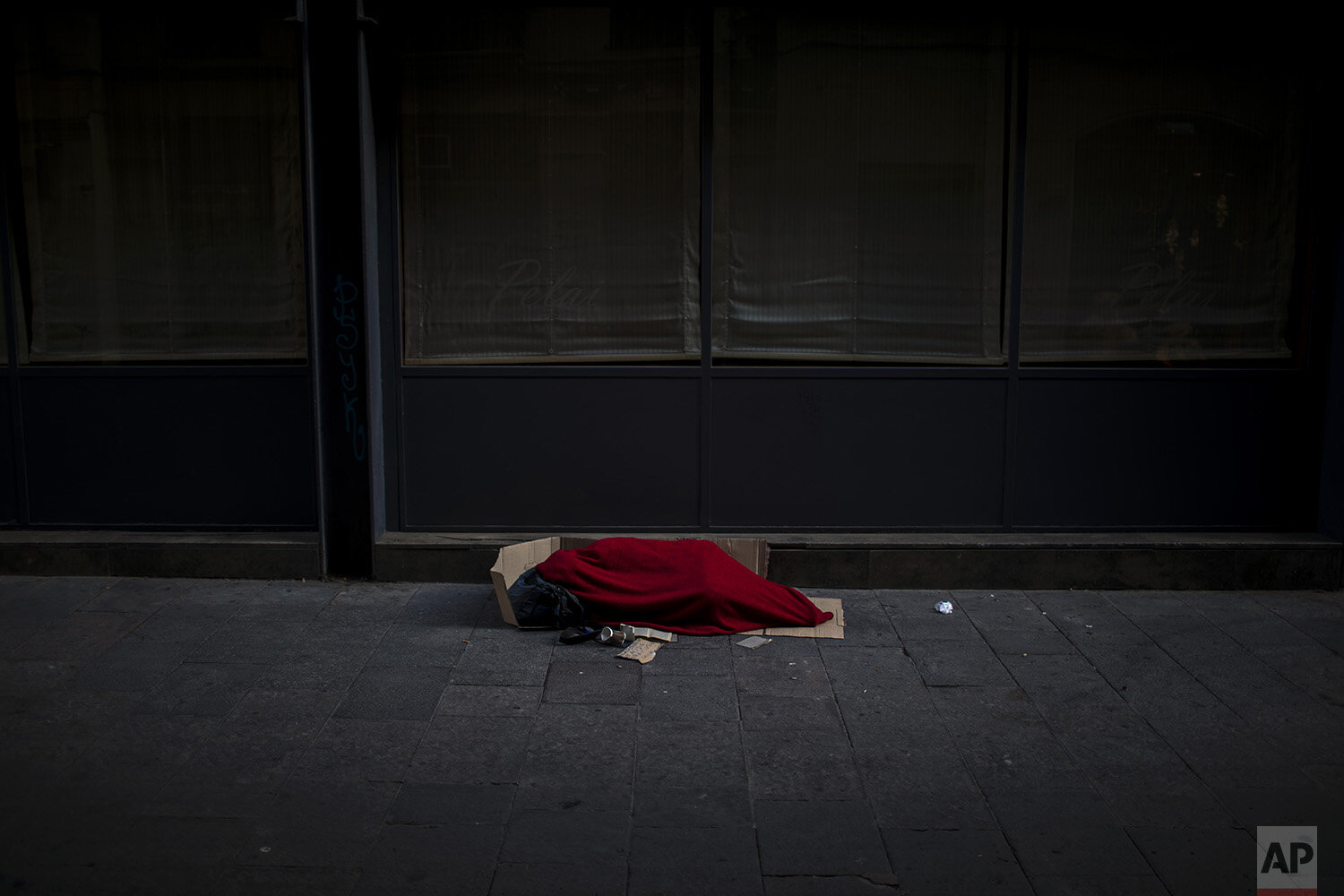  In this Sunday, March 22, 2020, a man covered with a blanket sleeps in an empty the street in Barcelona, Spain. In Barcelona sleeping figures with boxes and blankets punctuate the mostly empty city. They are Barcelona???s homeless, and there are abo