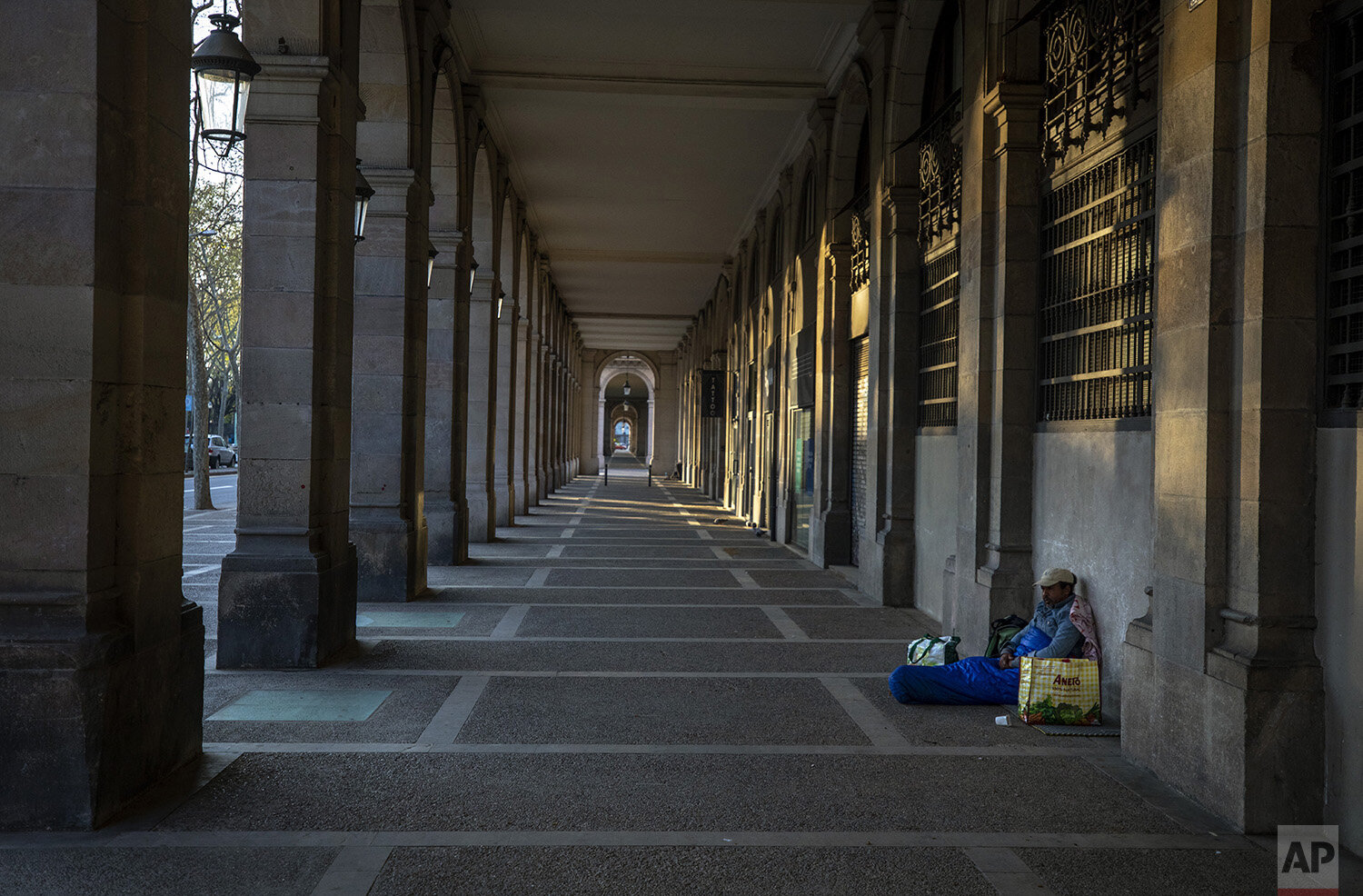 In this Friday, March 20, 2020, Riccardo, 32, sits in empty arcades in downtown Barcelona, Spain. "I thought I had seen everything during all these years sleeping in the street, but no. This silence on the street all day scares me... more than the v