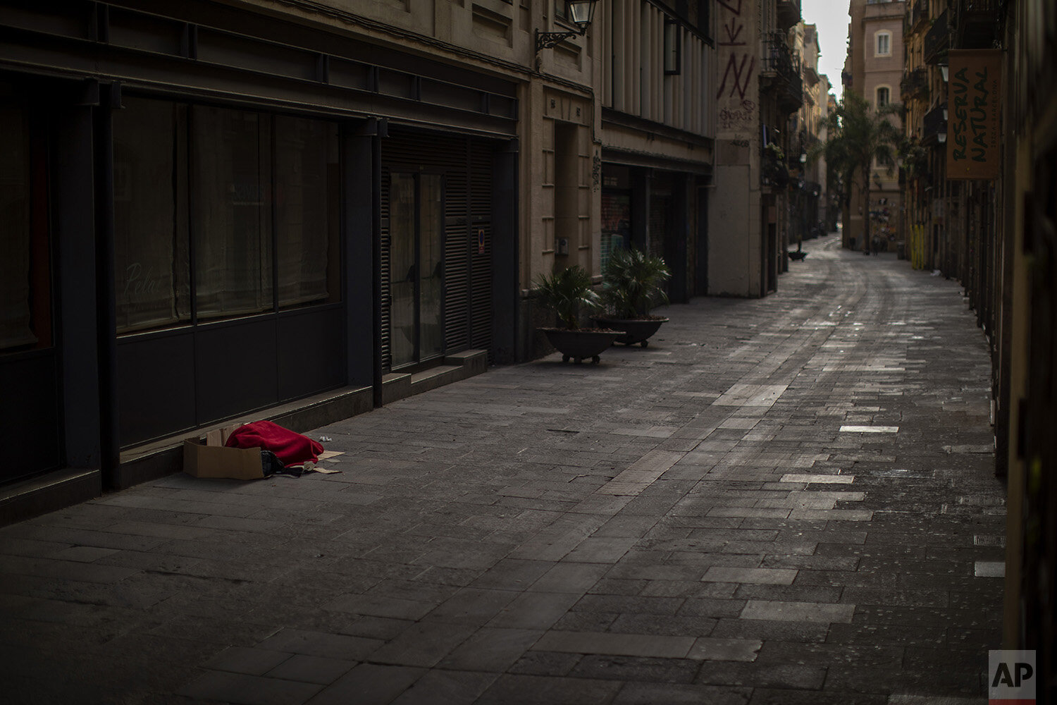  In this Sunday, March 22, 2020, a man covered with a blanket sleeps in an empty the street in Barcelona, Spain. In Barcelona sleeping figures with boxes and blankets punctuate the mostly empty city. They are Barcelona???s homeless, and there are abo