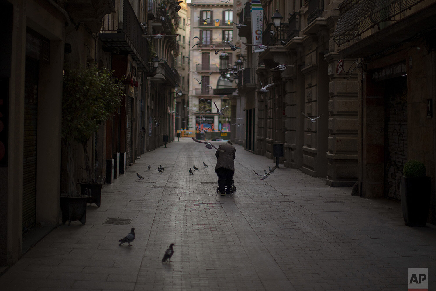  In this Saturday, March 21, 2020, a woman drags a cart with her belongings as she walks along an empty street in downtown Barcelona, Spain. (AP Photo/Emilio Morenatti) 