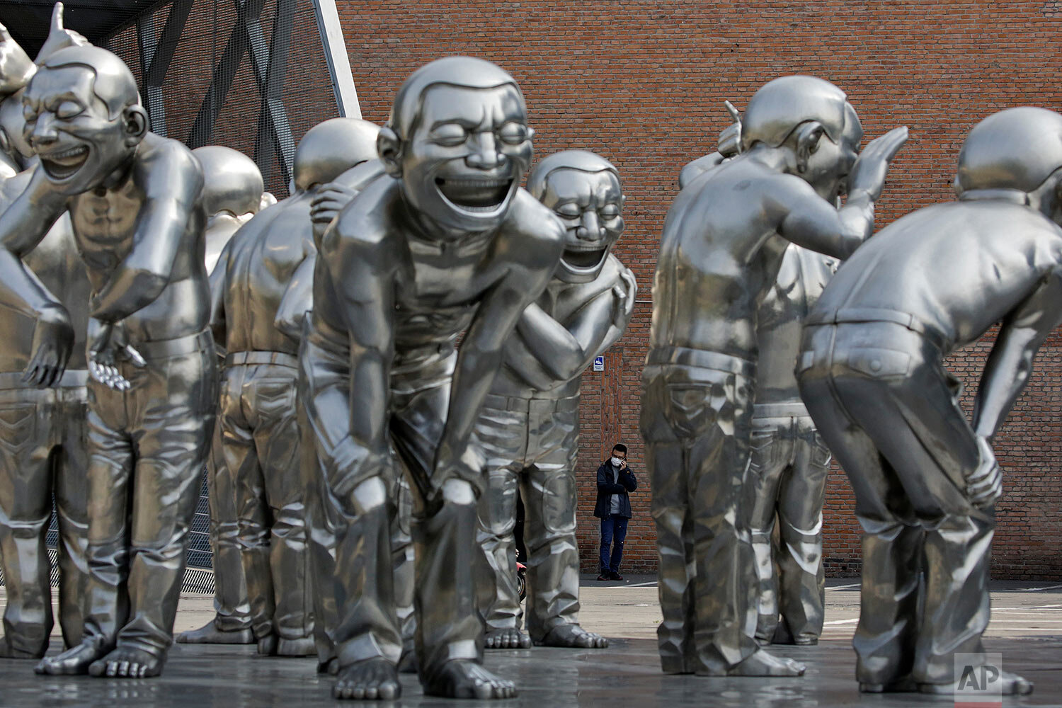  A man wearing a protective face mask to help curb the spread of the new coronavirus talks on his phone near the human sculptures on display outside an art gallery in Beijing, Tuesday, April 28, 2020. (AP Photo/Andy Wong) 
