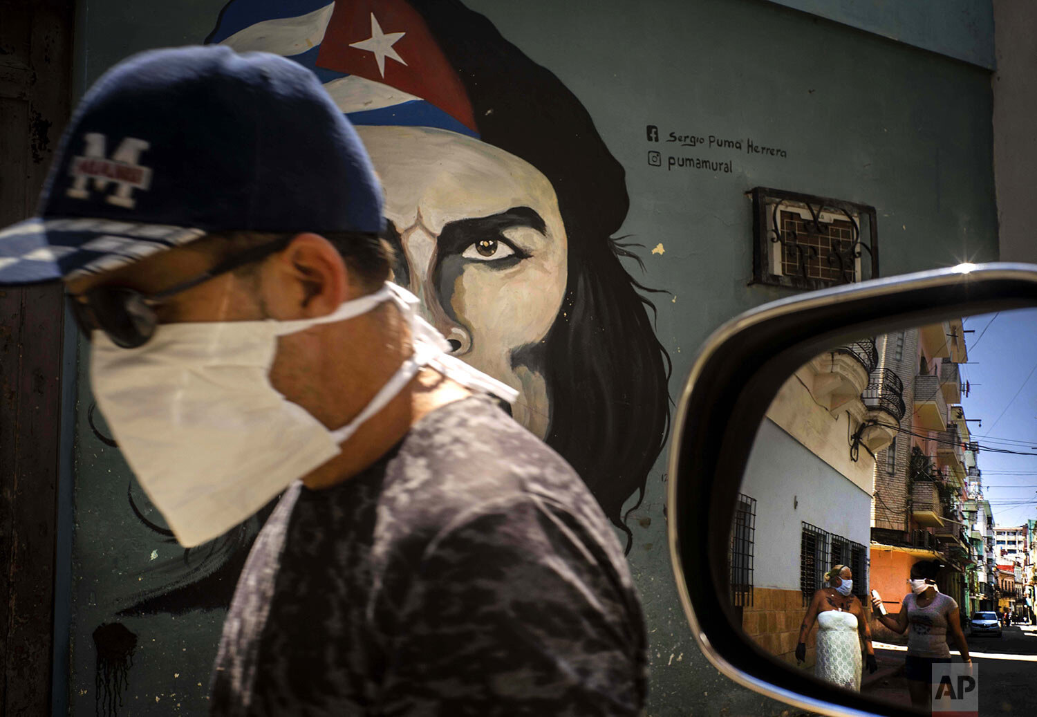  A man wearing a mask walks alongside a mural of Ernesto "Che" Guevara as other pedestrians are reflected in the side-view mirror of a car in Havana, Cuba, Tuesday, April 7, 2020. (AP Photo/Ramon Espinosa) 