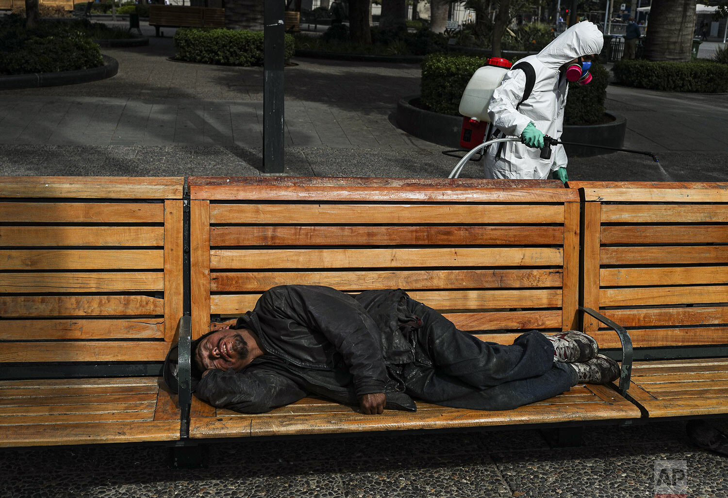  A city worker sprays disinfectant to help contain the spread of the new coronavirus near a man sleeping in the Plaza de Armas in Santiago, Chile, Wednesday, April 15, 2020. (AP Photo/Esteban Felix) 