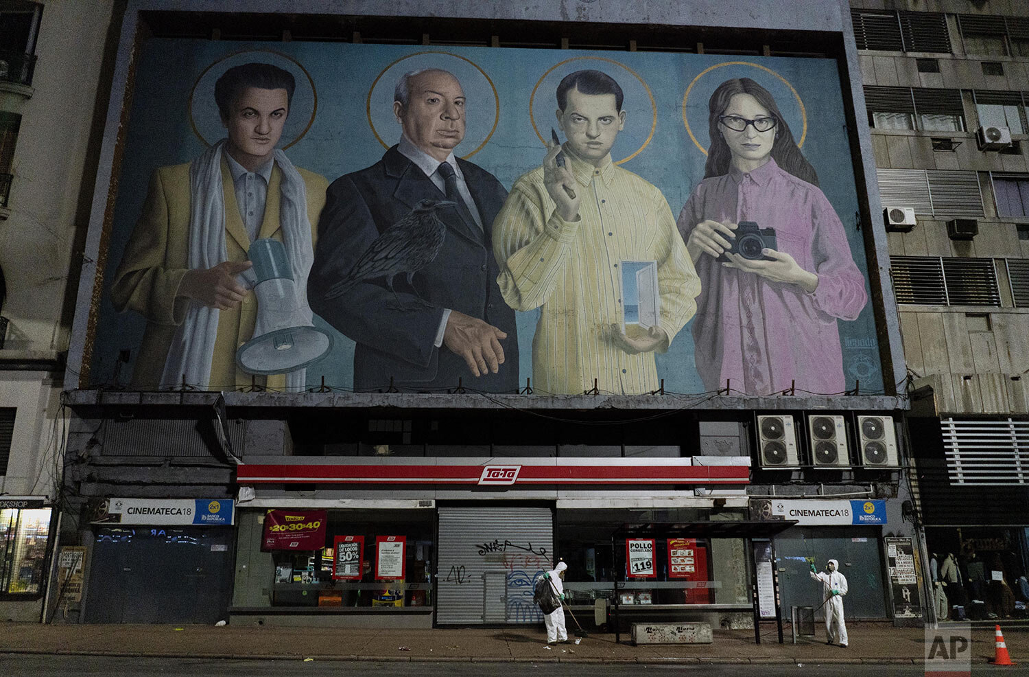  City workers disinfect a bus stop to help prevent the spread of new coronavirus outside a closed cinema featuring a mural of film directors, from left, Federico Fellini, Alfred Hitchcock, Luis Buñuel and Lucrecia Martel in Montevideo, Uruguay, just 