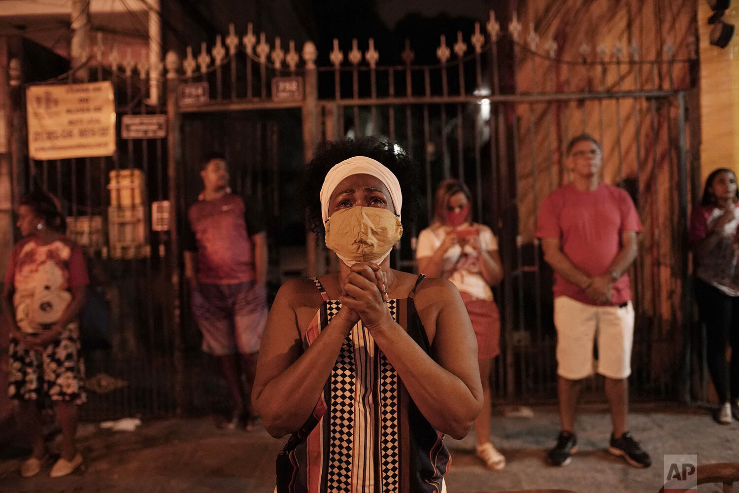  A woman wearing a mask as a precaution against the spread of the new coronavirus, prays illuminated by a street lamp outside the closed Saint George Church, to mark the feast day for Saint George, associated with bravery and resistance, in Rio de Ja