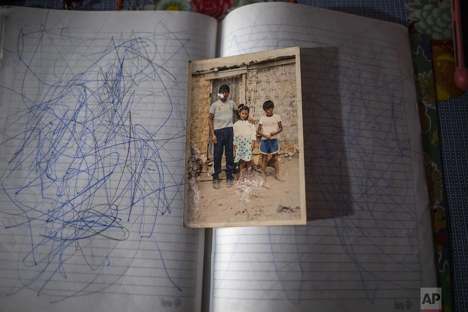  An old family snapshot of Jorge and Julia Lopez posing with their father Faustino Lopez, sits on a notebook of scribbled pages, in Lima, Peru, May 19, 2020. (AP Photo/Rodrigo Abd) 
