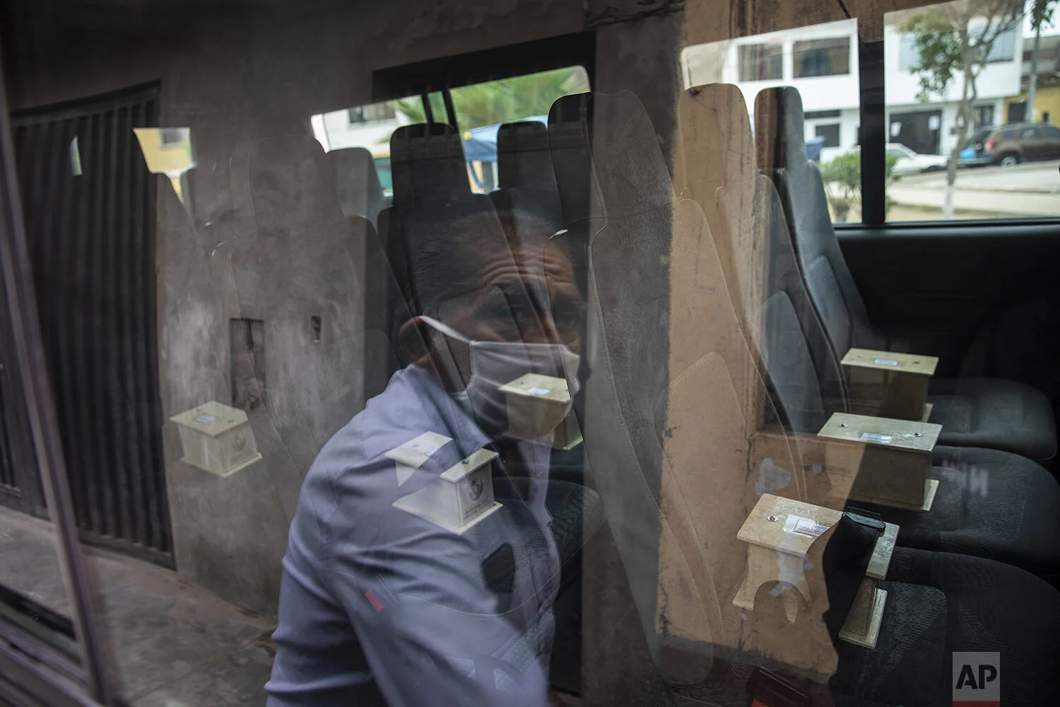  Piedrangel funeral home worker Anibal Rosado is reflected in a window of a company van as he prepares to help deliver to relatives, urns that contain the cremated ashes of people who are suspected to have died from the new coronavirus, in Lima, Peru