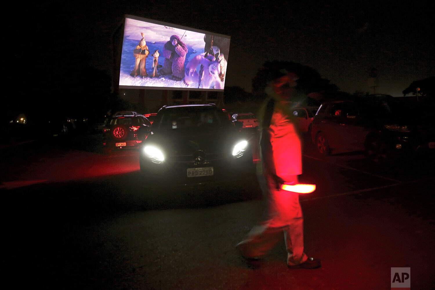  A worker carries a red lantern to signal drivers at the drive-thru movie theater amid the new coronavirus pandemic in Brasilia, Brazil, Wednesday, May 13, 2020. (AP Photo/Eraldo Peres) 