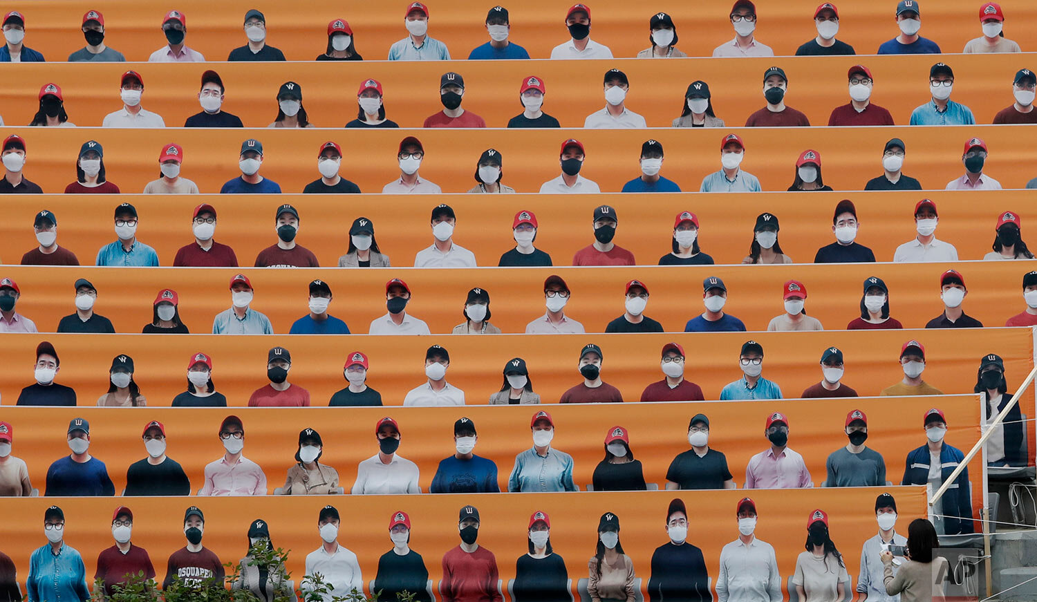  A woman holds her smartphone in front of the spectators' seats which are covered with pictures of fans, before the start of a baseball game between Hanwha Eagles and SK Wyverns in Incheon, South Korea, Tuesday, May 5, 2020. (AP Photo/Lee Jin-man) 