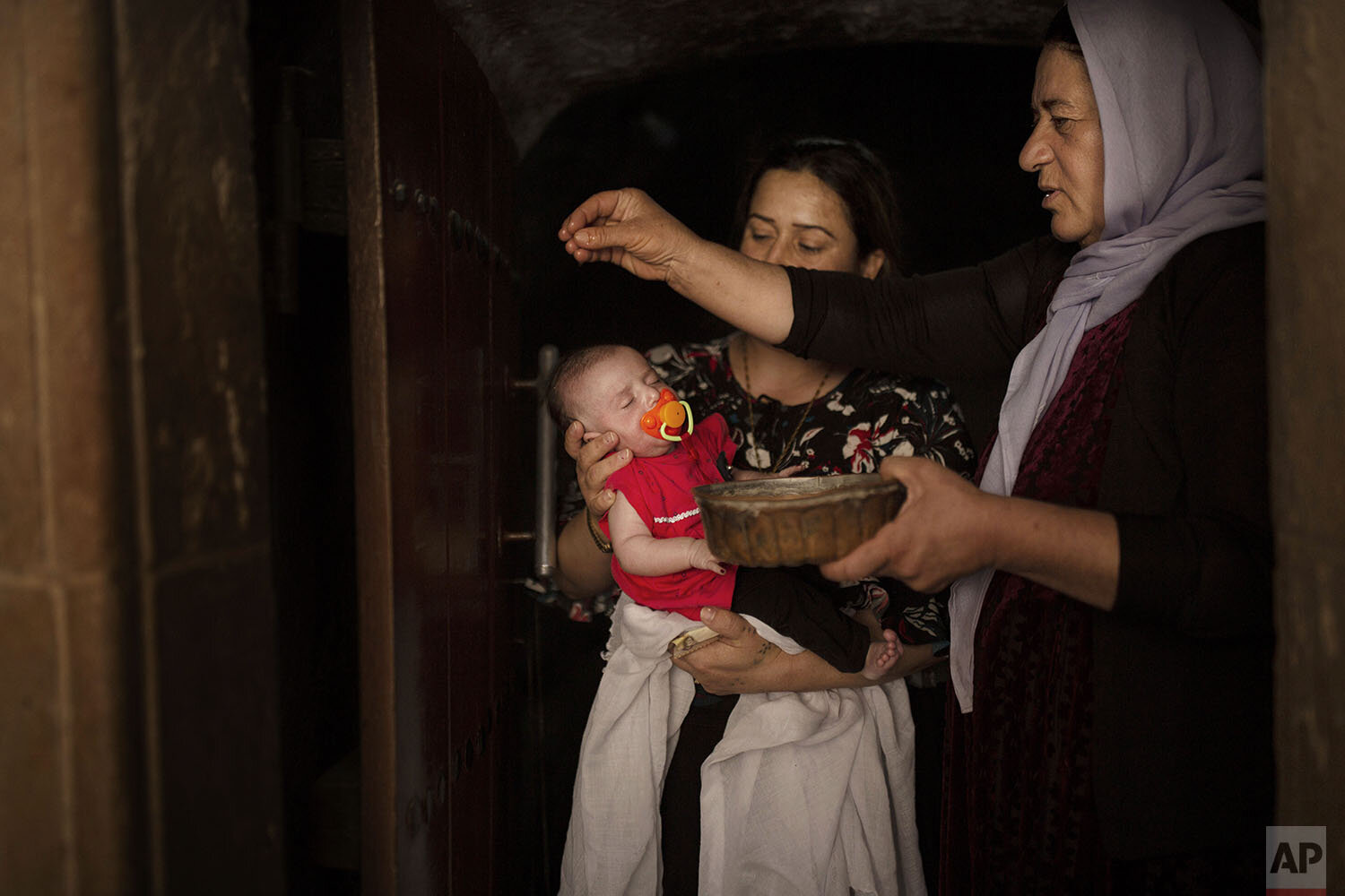 In this Aug. 23, 2019, photo, a baby girl is water from an ancient spring by a Yazidi holy woman at the the Lalish temple near Sheikhan, Iraq. The ancient sect is rebuilding, nearly six years after Islamic State militants launched its coordinated at
