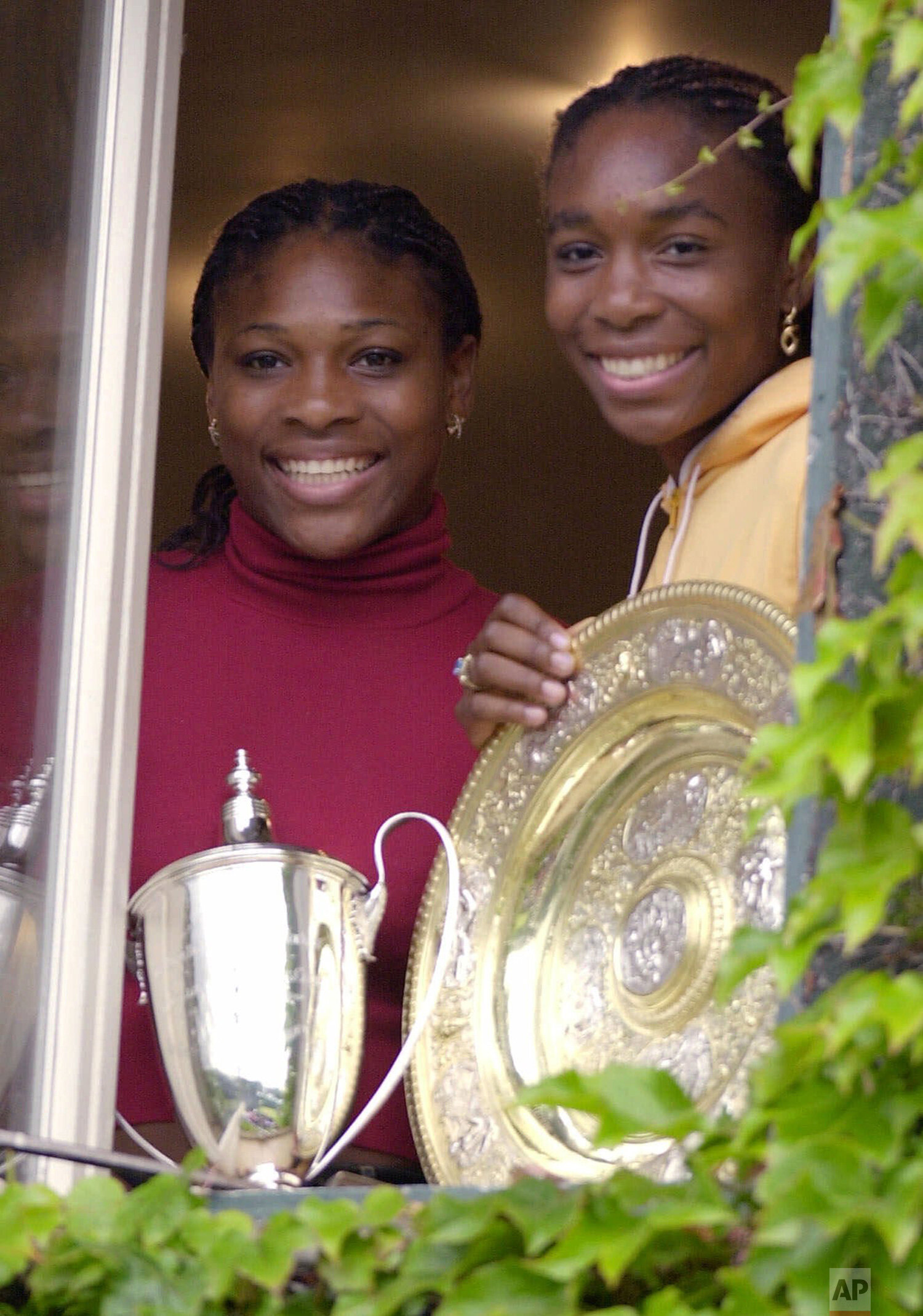  Venus Williams, right, displays the women's singles trophy and her sister Serena displays the women's doubles trophy from a window in the women's locker room in the Centre Court complex at Wimbledon, Monday, July 10, 2000. Venus Williams and her sis