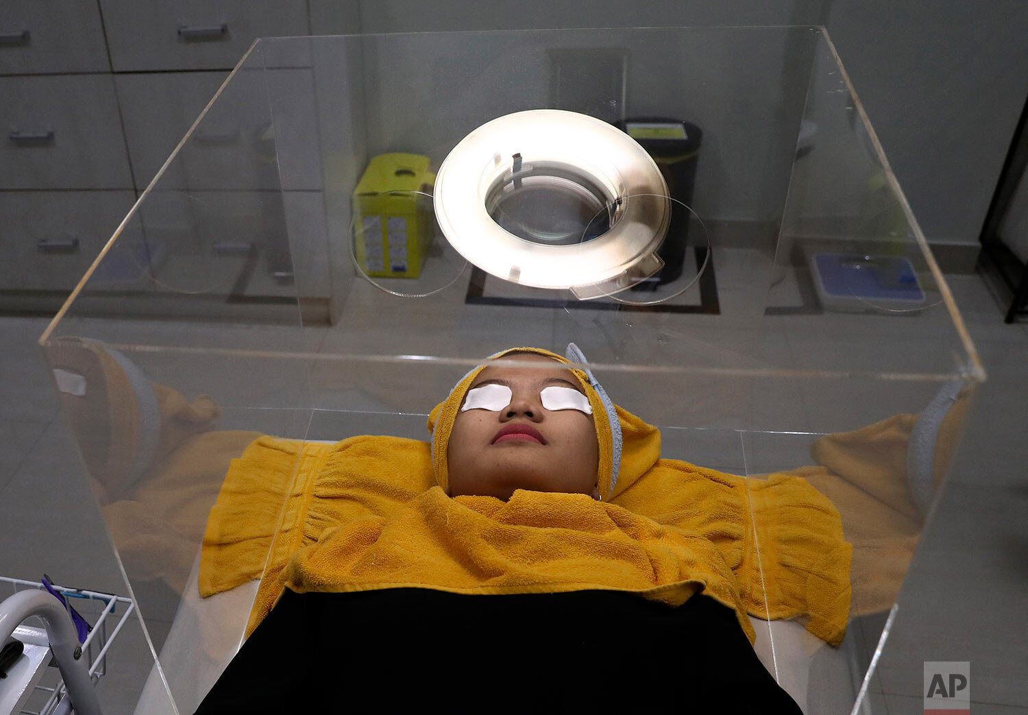  A patient waits for treatment inside a protective acrylic box used as a precaution against the new coronavirus outbreak at the beauty clinic at Tambak Hospital in Jakarta, Indonesia, Tuesday, June 23, 2020. (AP Photo/Tatan Syuflana) 
