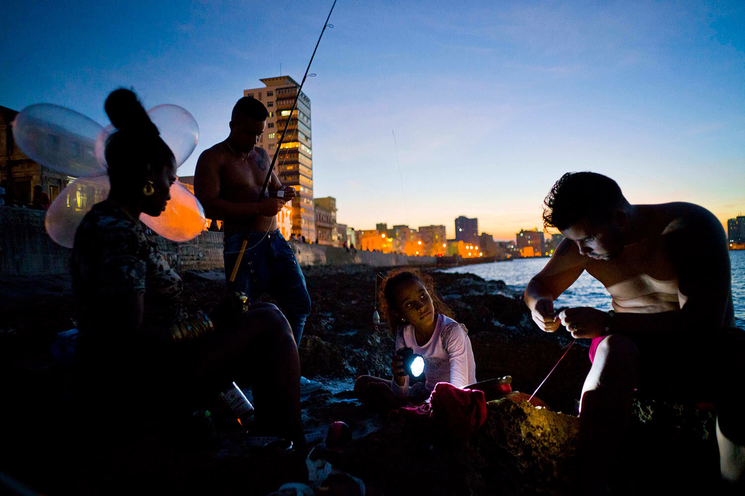  In this Nov. 13, 2016 photo, Edelmis Ferro Solano, far left, holds inflated condoms for her husband Junior Torres Lopez, standing behind her, to use on his fishing line as a bobber, while her granddaughter Leyanis Macias Puente helps out by shining 