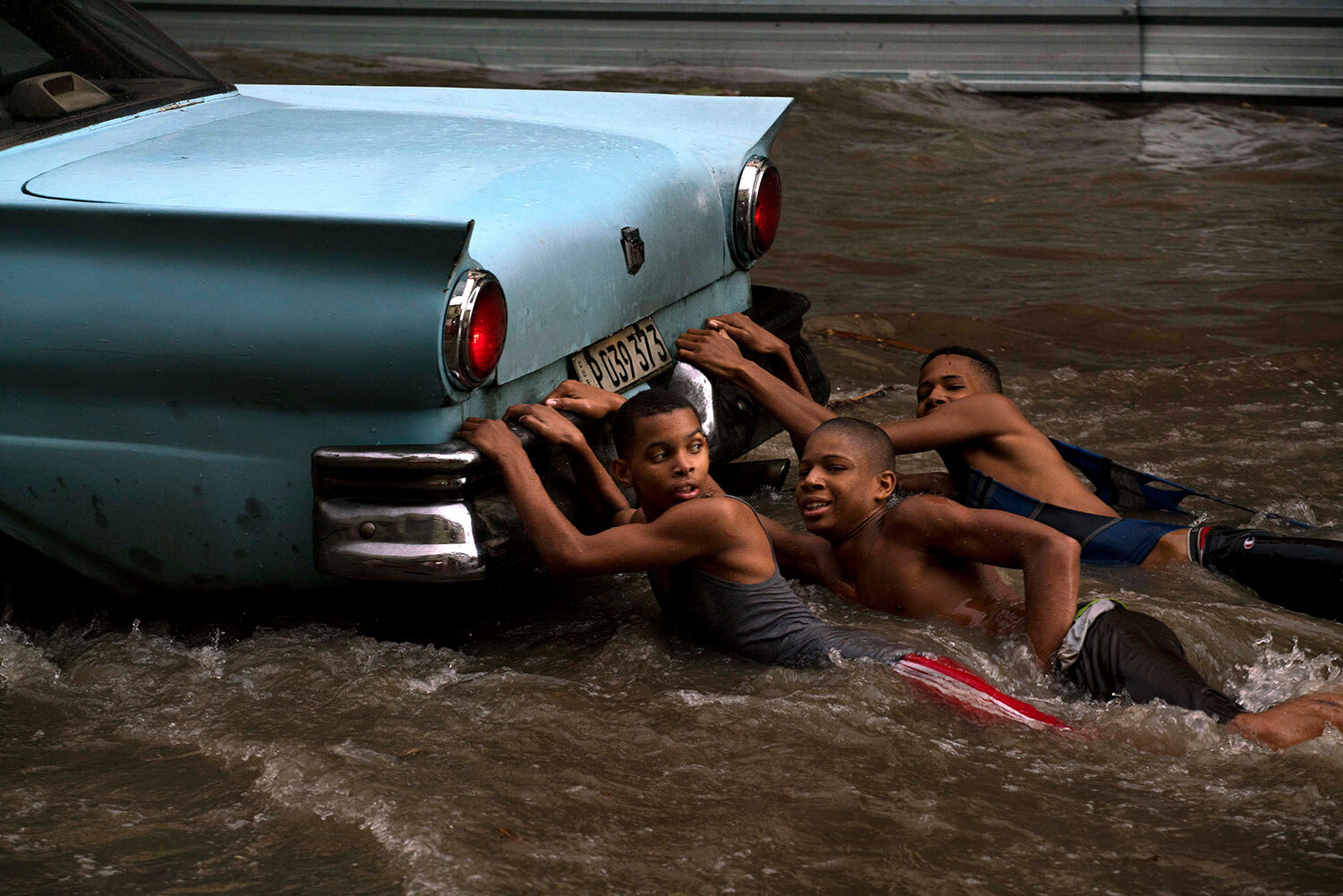  Youths hang from the rear bumper of a vintage American car as they play in a flooded street, after a heavy rain in Havana, Cuba, Wednesday, Oct. 14, 2015. (AP Photo/Ramon Espinosa) 