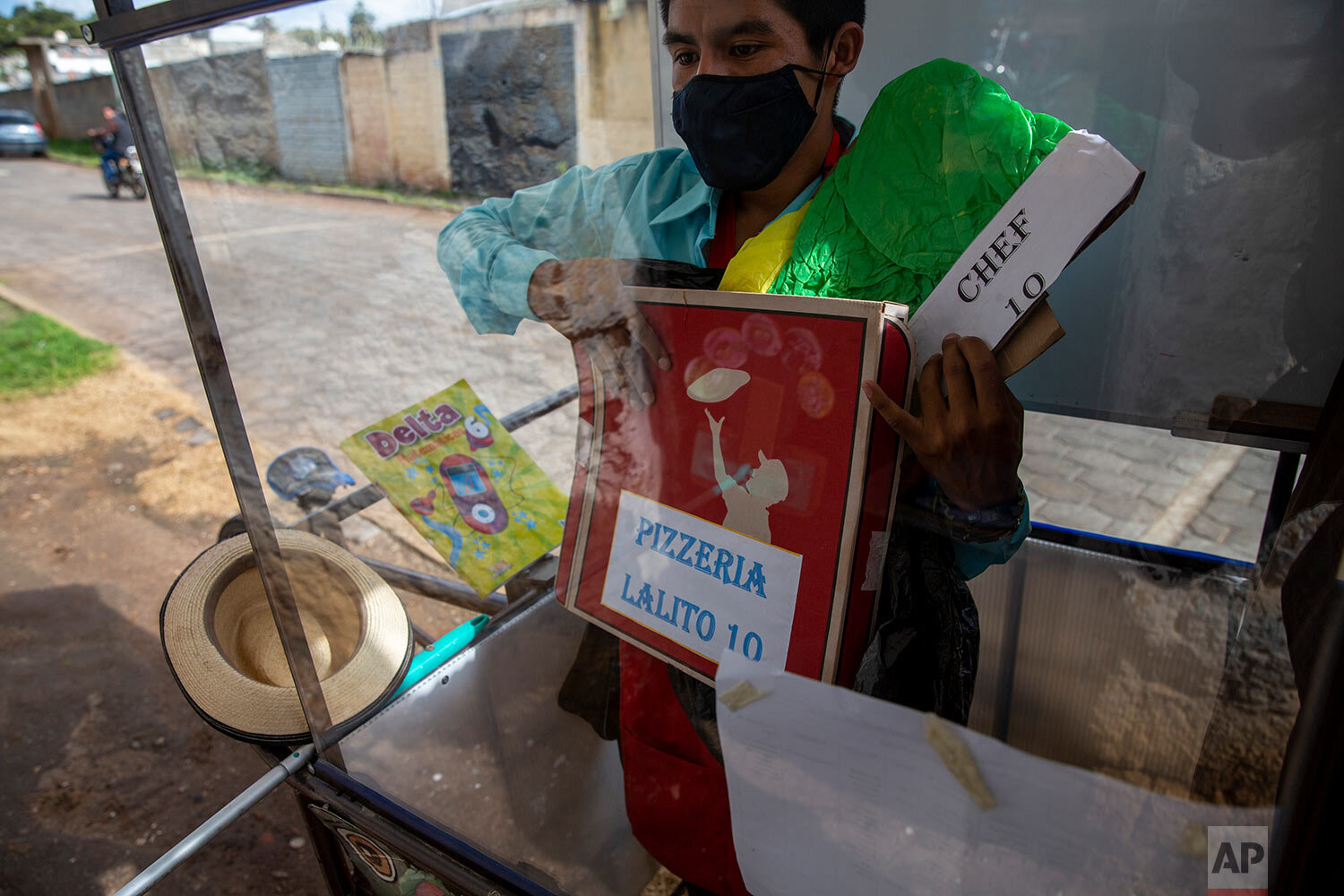  Standing behind the plexiglass window of his mobile classroom, Gerardo Ixcoy holds a pizza box as part of a lesson on fractions, in Santa Cruz del Quiche, Guatemala, Wednesday, July 15, 2020. "I tried to get the kids their work sheets sending instru