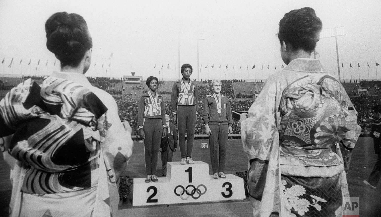  Japanese girls in ceremonial kimonos frame the winner's stand after the presentation of medals for winners of the women's Olympic 100-meter race, on Oct. 16, 1964, in Tokyo. On the podium are American gold medalist Wyomia Tyus, center; teammate Edit