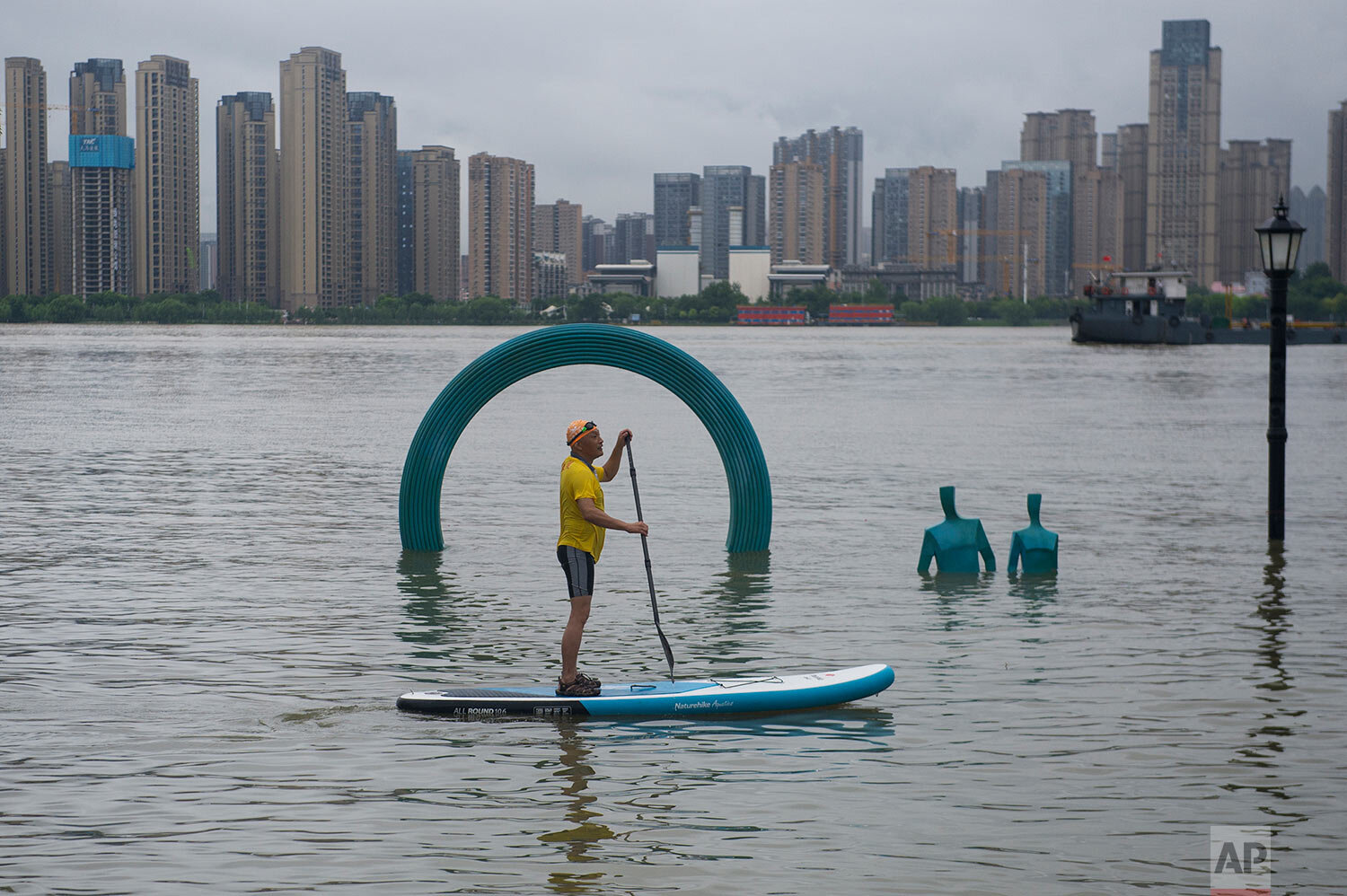  A man paddles by a sculpture submerged by floodwaters along the riverside park in Wuhan in central China's Hubei province Sunday, July 5, 2020.  (Chinatopix via AP) 
