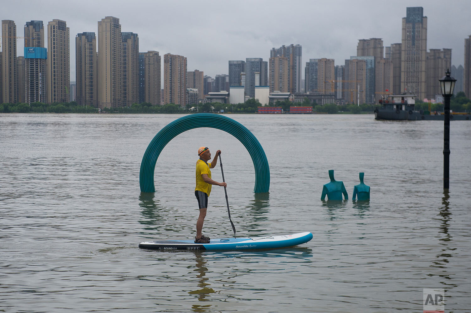 A man paddles by a sculpture submerged by floodwaters along the riverside park in Wuhan in central China's Hubei province Sunday, July 5, 2020. (Chinatopix via AP)