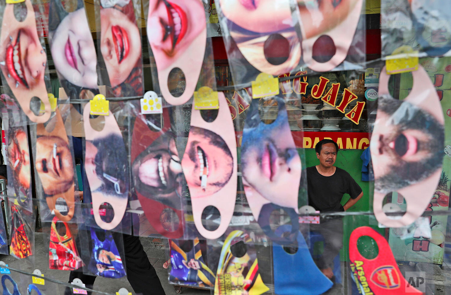  A man is seen through a display of fun face masks for sale at a roadside stall in Jakarta, Indonesia, Thursday, July 16, 2020. (AP Photo/Achmad Ibrahim) 