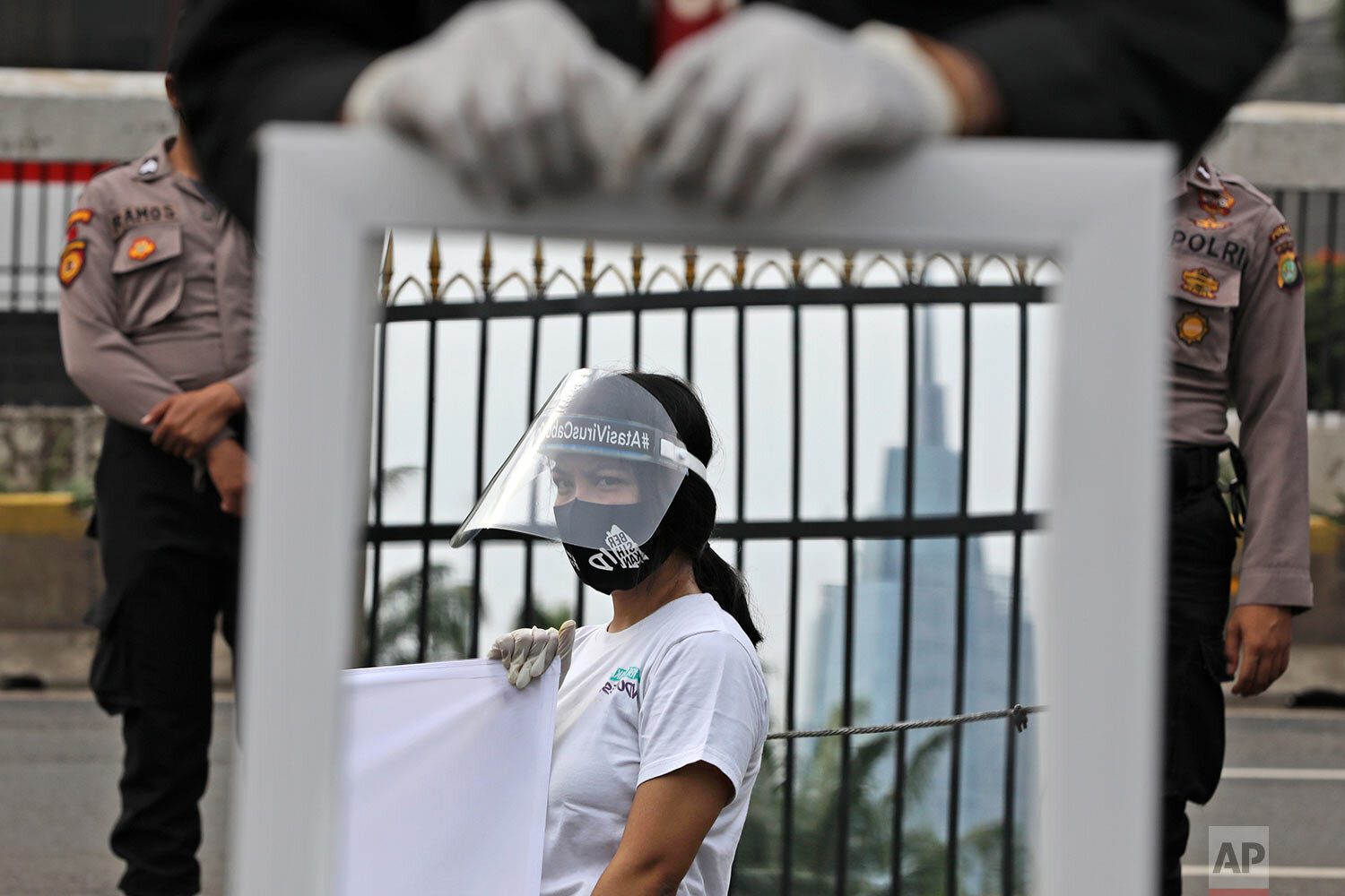  A mirror reflects the image of an activist wearing a mask and protective face shield as a precaution against the new coronavirus outbreak during a small protest outside the parliament in Jakarta, Indonesia, Tuesday, July 14, 2020. (AP Photo/Dita Ala