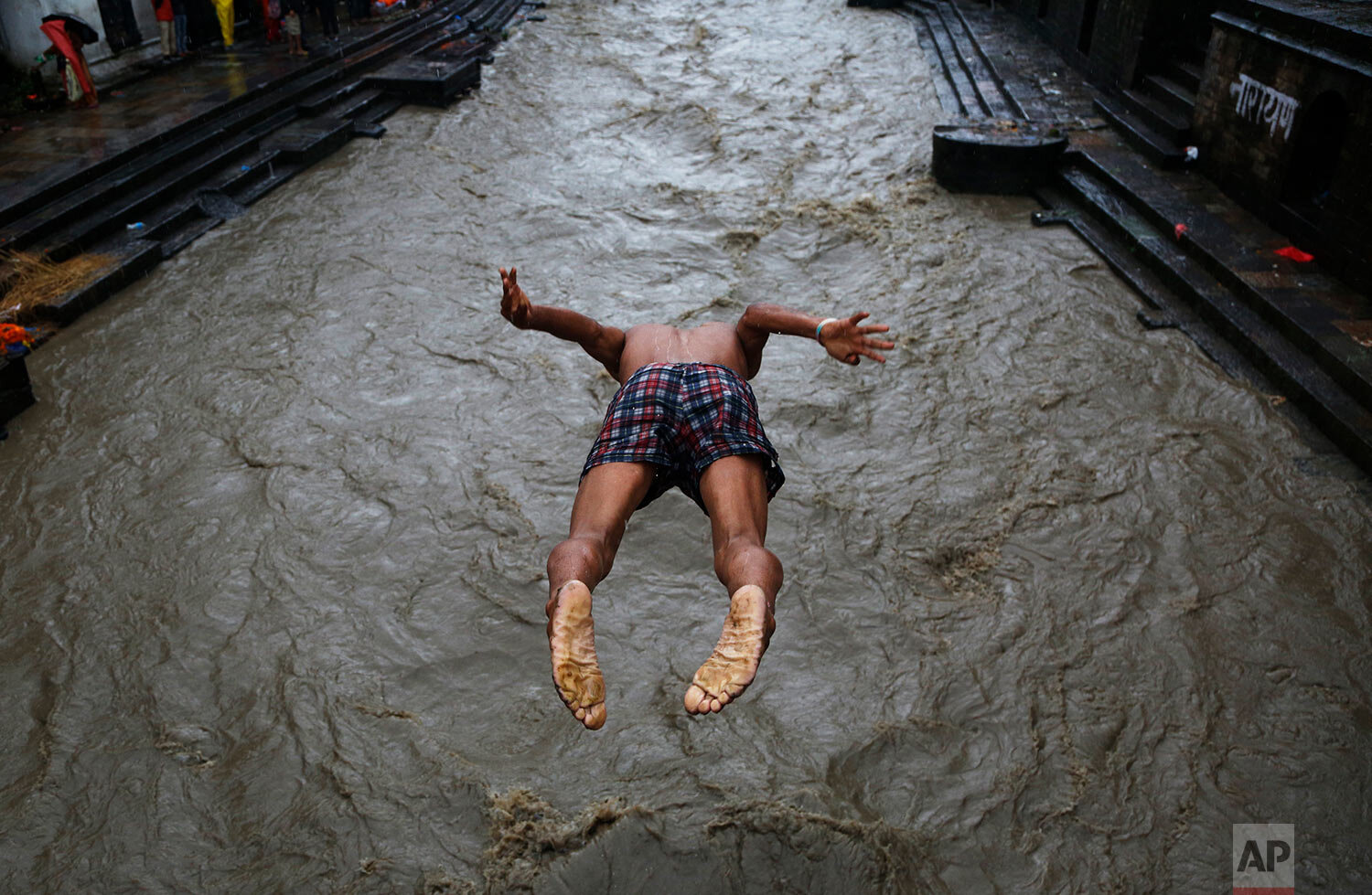 A Nepalese man jumps into the Bagmati river during monsoon rains in Kathmandu, Nepal, Monday, July 20, 2020. (AP Photo/NIranjan Shrestha)