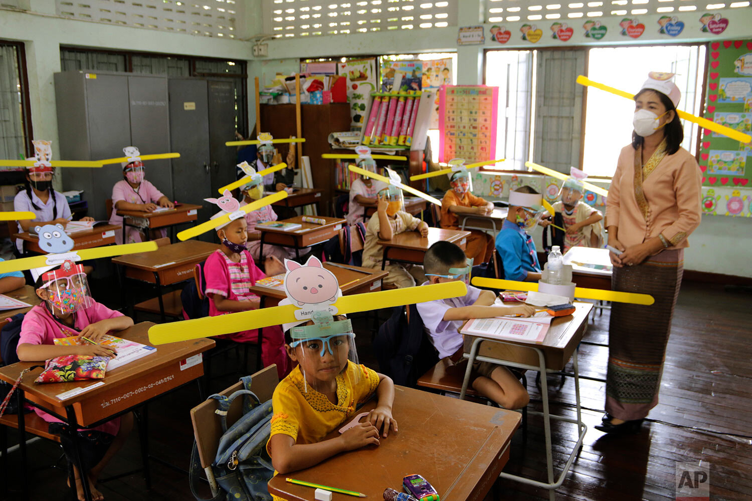 A teacher and students wearing hats designed for space keeper, practice social distancing to help curb the spread of the coronavirus at Ban Pa Muad School in Chiang Mai, north of Thailand, Friday, July 3, 2020. (AP Photo/ Wichai Taprieu)