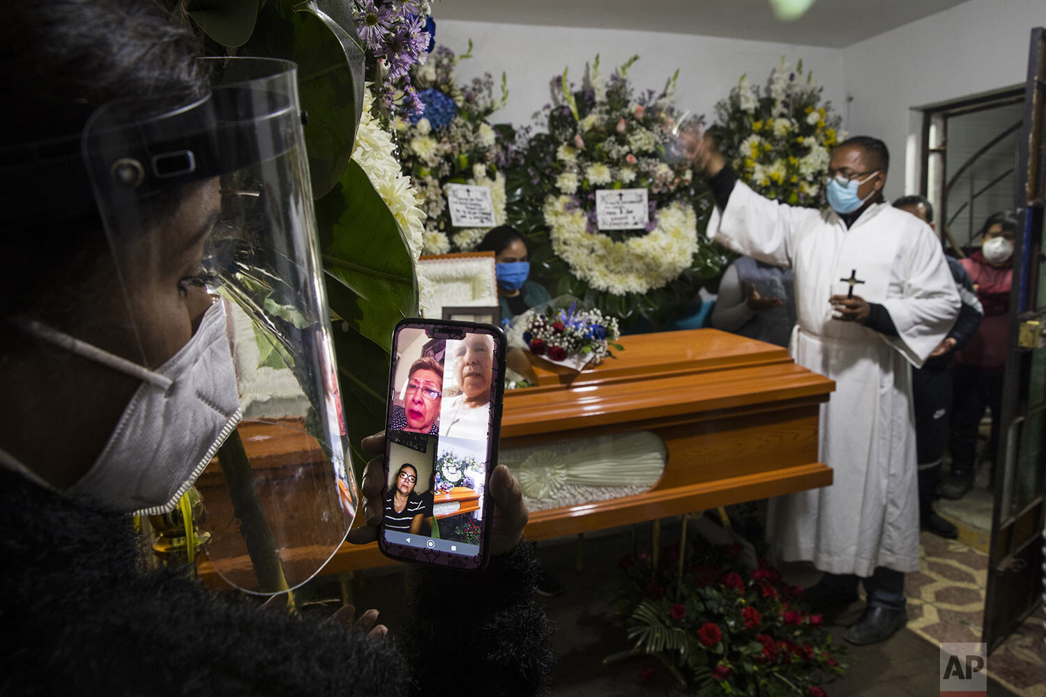  Brother Ronald Marin sprinkles holy water on the coffin that contains the remains of 97-year-old Ruben Val, as granddaughter Leslie Gonzalez holds her cell phone in place so that her parents can take part in the service via video conferencing in Com