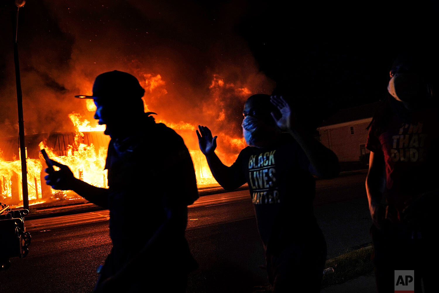  Protesters walk past police with their arms up, late Monday, Aug. 24, 2020, in Kenosha, Wis., as a building burns in the background. (AP Photo/David Goldman) 