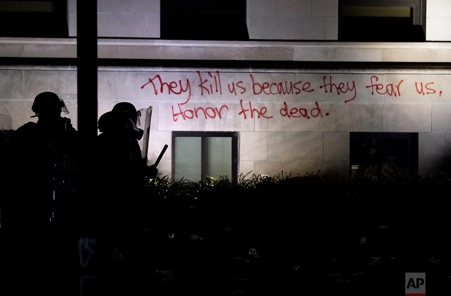  Police in riot gear stand in a line against protesters next to a message spay painted on the Kenosha County Courthouse, late Monday, Aug. 24, 2020, in Kenosha, Wis. (AP Photo/David Goldman) 