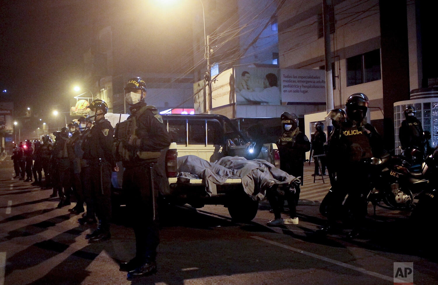  Police stand guard by two bodies  in a truck outside a disco in Lima, Peru, Aug. 23, 2020, after a dozen people died in a stampede after a raid to enforce the COVID-19 lockdown. (AP Photo/Diego Vertiz) 